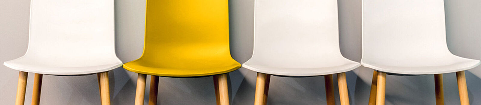 An einer Wand stehen vier Stühle in Weiß und Gelb.